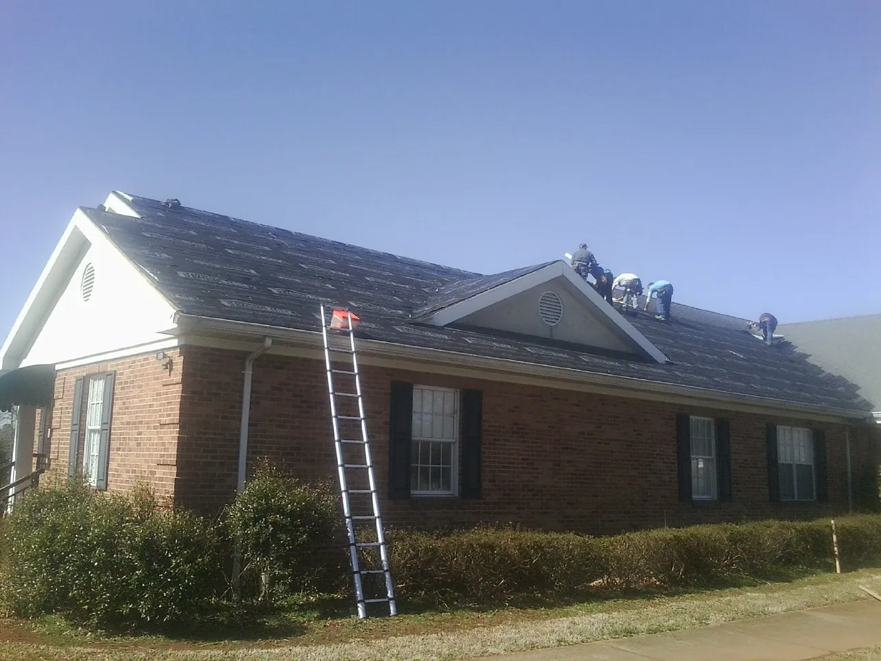 Crew tearing shingles off a brick ranch roof with a ladder set — Metal Roof Repair work by our crew in Newington
