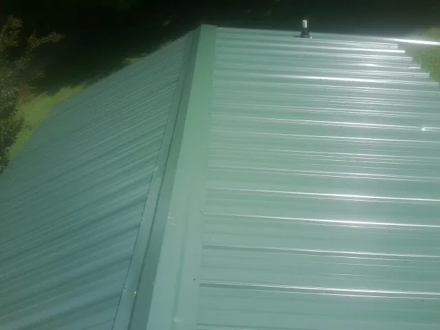 New green metal panels meeting at the ridge of a roof — Flat Roof Repair work by our crew in Newington