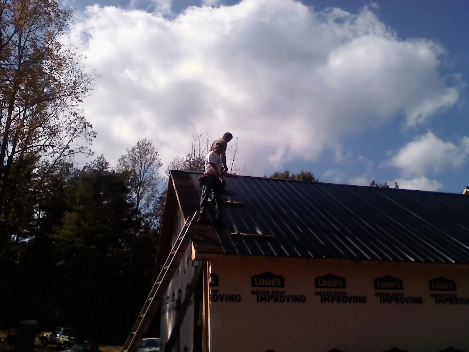 Roofer fastening dark metal panels high against a cloudy sky, from a Roof Inspection job in Newington