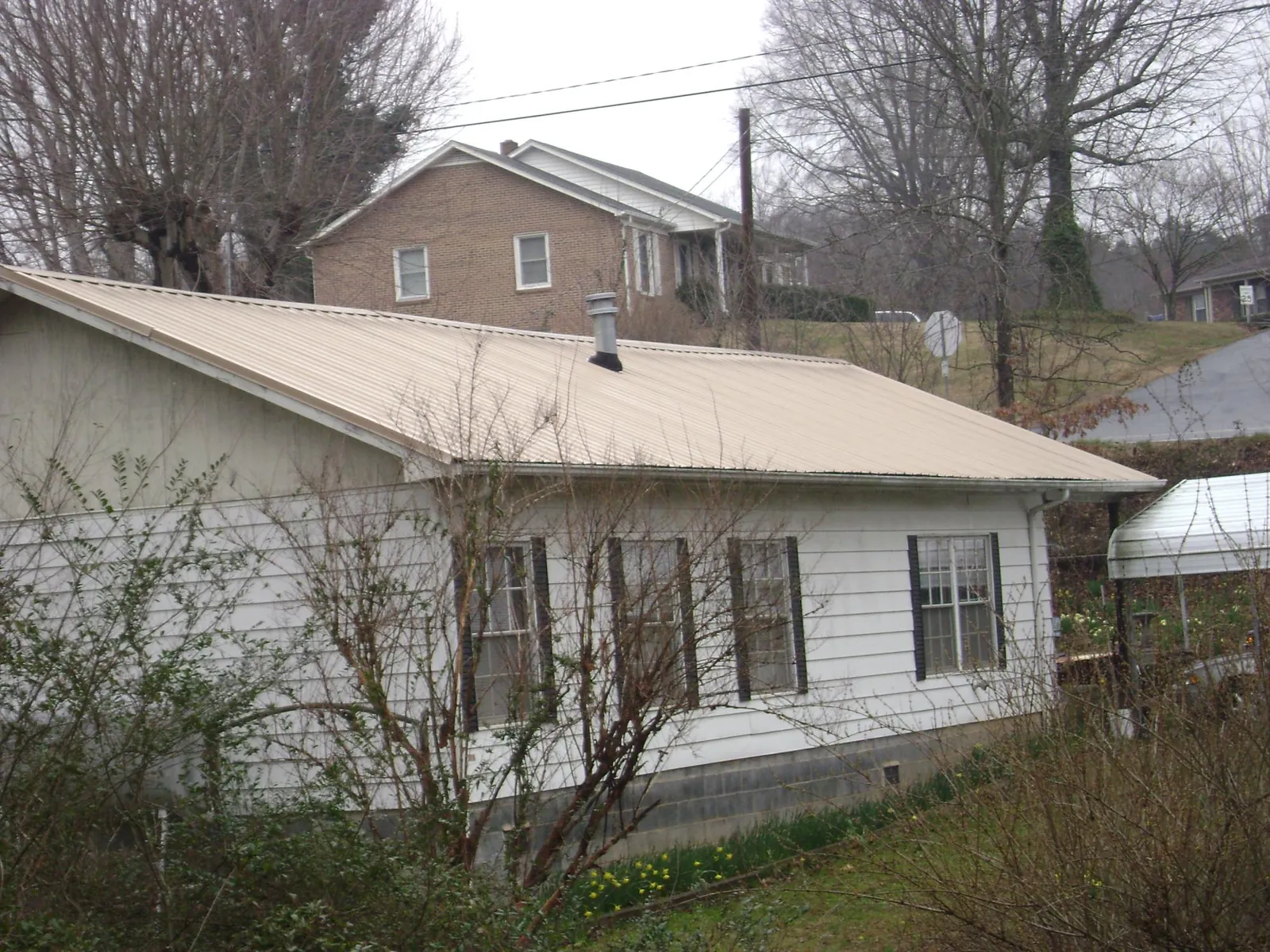 Tan metal roof on a white sided house set into a hillside — Commercial Roofing by Roofing Brothers in Newington