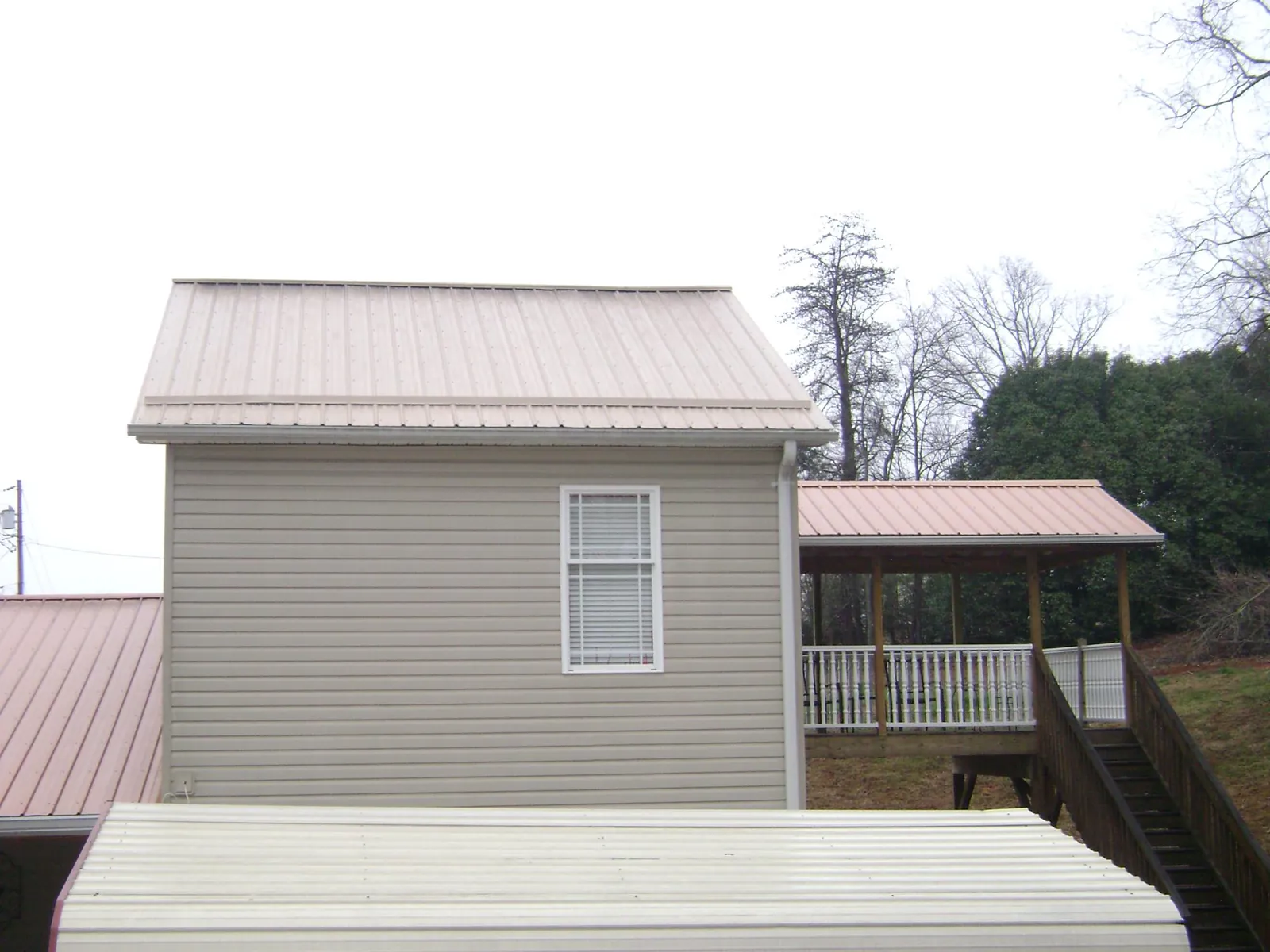 Tan metal roofs on a two story addition and attached porch, from a Roof Replacement job in Newington